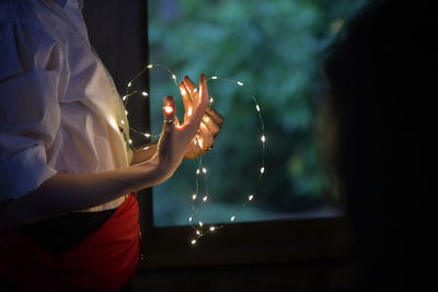 Midsection of woman holding illuminated fire at night