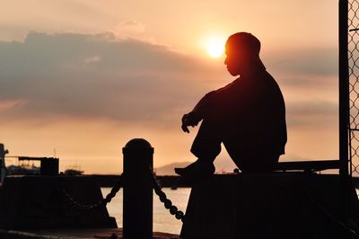 Silhouette man standing by sea against sky during sunset