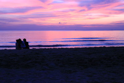 Silhouette people sitting at beach against sky during sunset