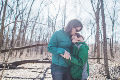 Mother embracing son while standing in forest