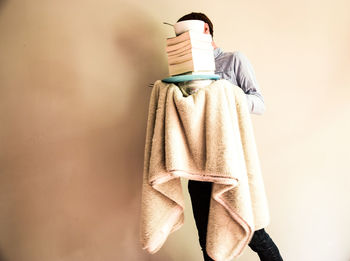 Man carrying stacked books with towel against beige wall