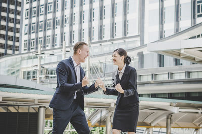 Happy business people gesturing while standing against building