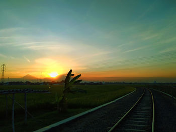 Railroad tracks on field against sky during sunset