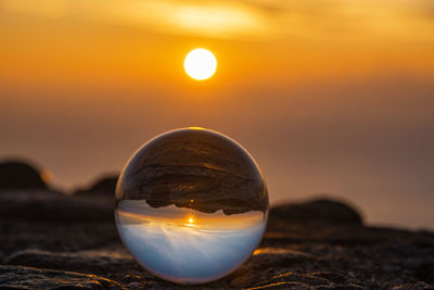 Close-up of crystal ball on beach against sky during sunset