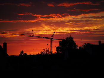 Silhouette cranes against orange sky during sunset