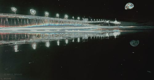 Illuminated city by lake against sky at night