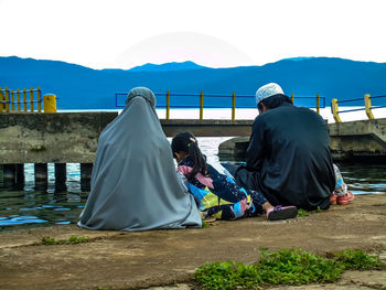 Rear view of couple sitting on mountain against sky