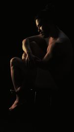 Full length of naked man sitting against black background