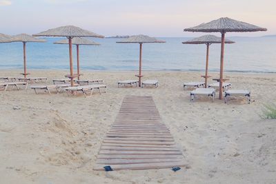 Deck chairs and parasols on empty beach against sky and light blue sea