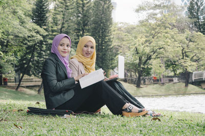 Female friends in hijab using laptop by lake