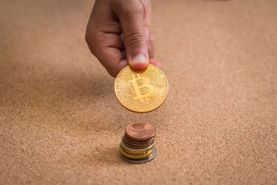 Close-up of hand holding bitcoin over stack on table