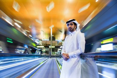 Man standing amidst blurred motion of light trails at railroad station