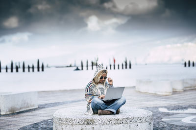 Woman sitting on rock by sea against sky