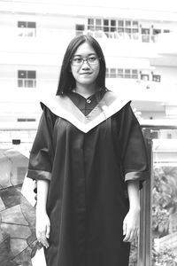 Young woman in graduation gown standing against building