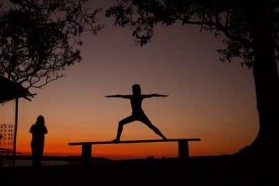 Silhouette woman standing by tree against sky during sunset