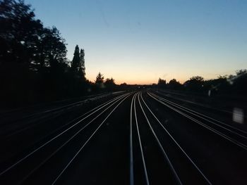 Railroad tracks by silhouette trees against clear sky