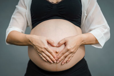 Midsection of woman touching face against gray background