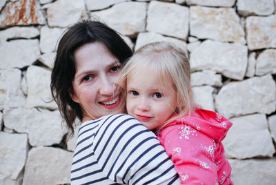 Portrait of young woman with daughter standing against wall