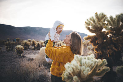 A woman with a baby is standing near a cactus in the desert