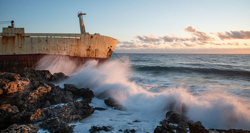  scenic view of an abandoned ship in the stormy sea with big wind waves during sunset.