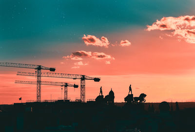 Silhouette cranes at construction site against sky during sunset