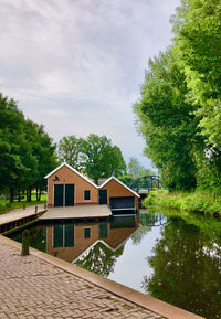 House by lake and buildings against sky