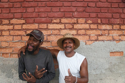 Portrait of man with friend standing against brick wall