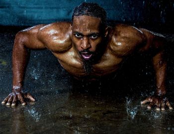 Portrait of shirtless man doing push-ups in rain