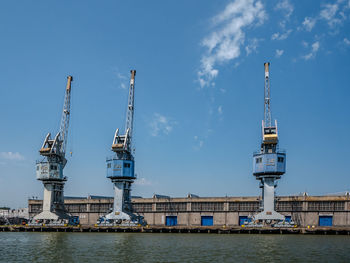 Cranes at harbor against sky