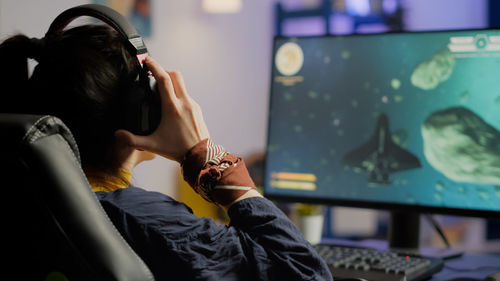 Rear view of woman playing video game at home