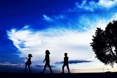 Silhouette people standing against blue sky