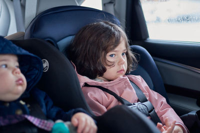 Siblings in car seats having snacks in the back seat of a car on a rainy day