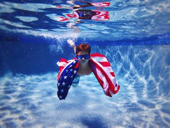 Portrait of cute boy with american flag swimming under pool