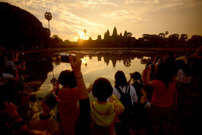 People photographing against lake and sky during sunset