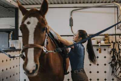 Woman in stable putting saddle on horse