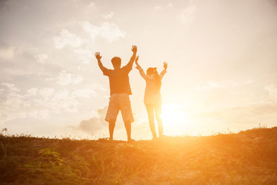 Low angle view of friends standing against sky during sunset