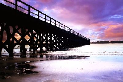 Bridge over calm sea against cloudy sky