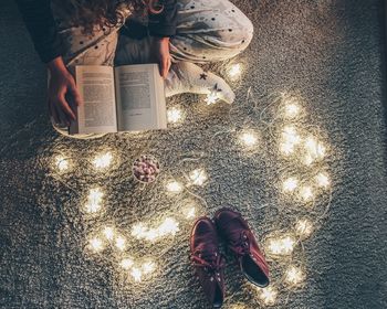 High angle view of woman reading book by illuminated lights with shoes