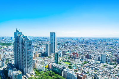 Aerial view of buildings in city against blue sky