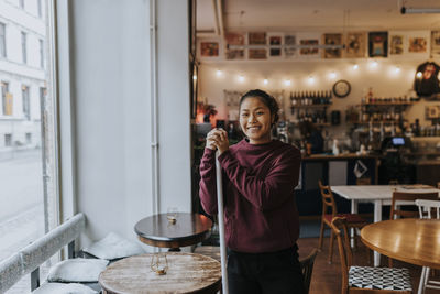 Portrait of happy female owner standing by table in coffee shop