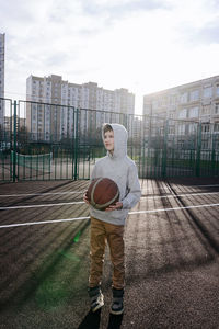 Teenager with basketball ball standing on court 