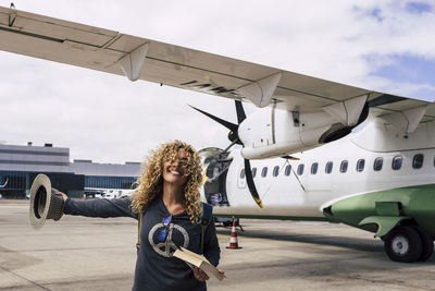 Woman standing by airplane on runway against sky