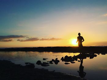 Rear view of silhouette man standing at beach against sky during sunset