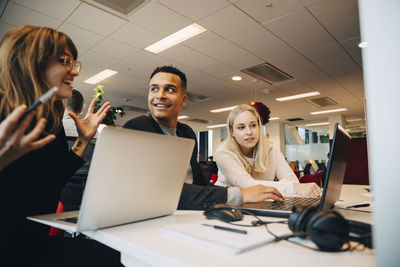 Smiling businesswoman discussing with colleagues sitting at desk in office