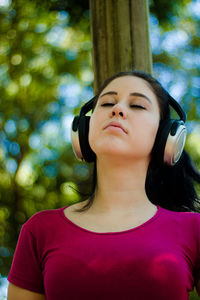 Low angle view of young woman with eyes closed listening music while standing at park