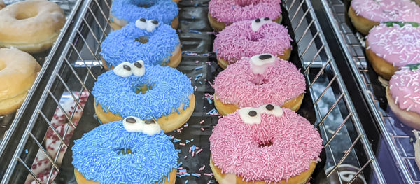 American blue and pink donuts with a smile and eyes lie in a metal tray in a store, side view.