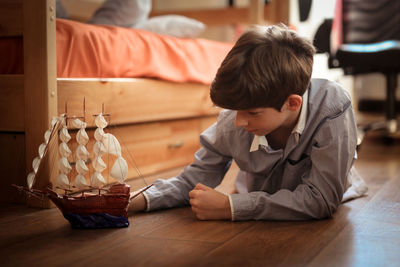 Boy teen plays with ship model on the floor in real children's room