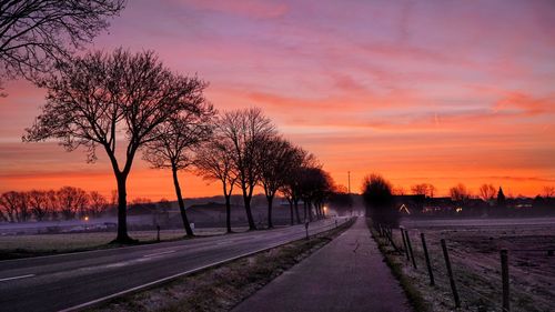 Road by trees against romantic sky at sunset