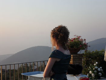 Young woman standing on a terrace against clear sky