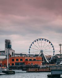 Ferris wheel by river against sky during sunset